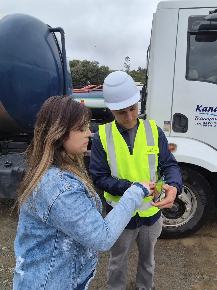 Cliente assina no celular do técnico, ao lado do caminhão, no local do serviço.