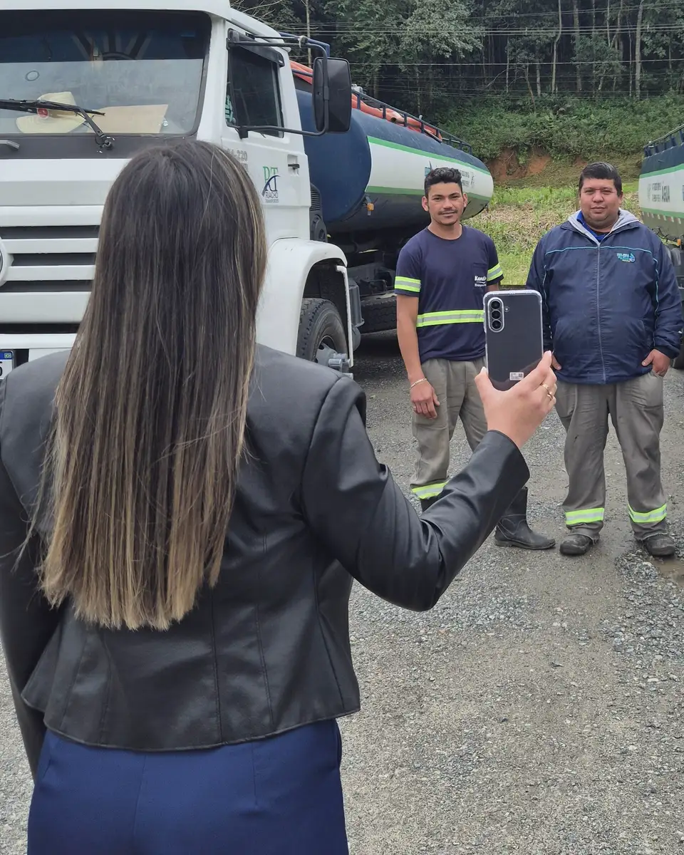 No pátio da Kandir Transportes, uma pessoa fotografa a equipe entre dois caminhões-pipa.